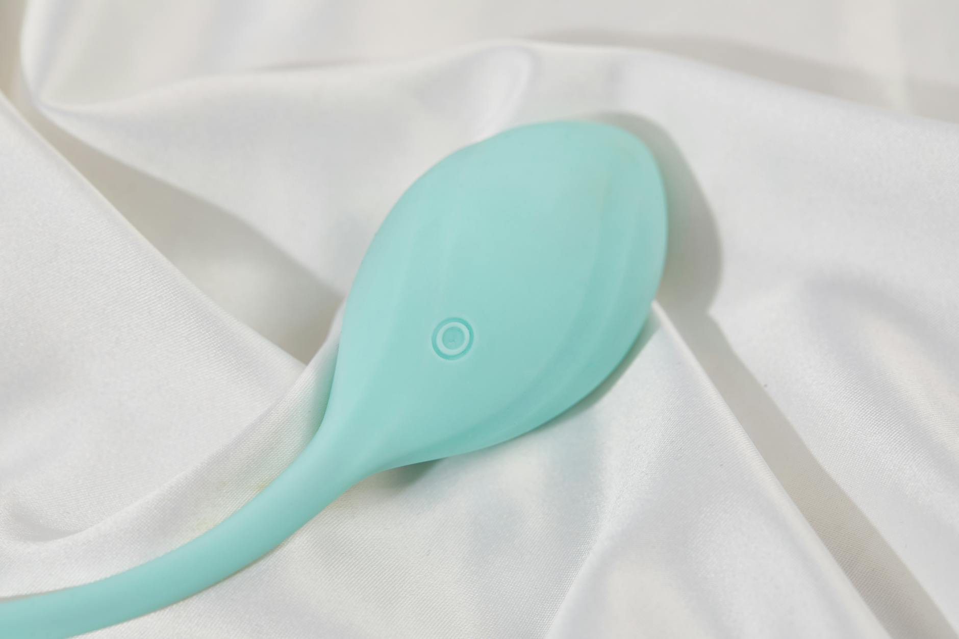 A teal silicone vibrator on smooth white fabric representing modern intimate wellness