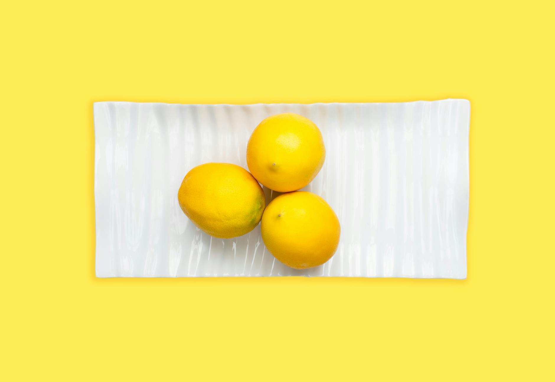 A blue vibrator surrounded by citrus and flowers on a yellow background, suggesting joy and extended pleasure.
