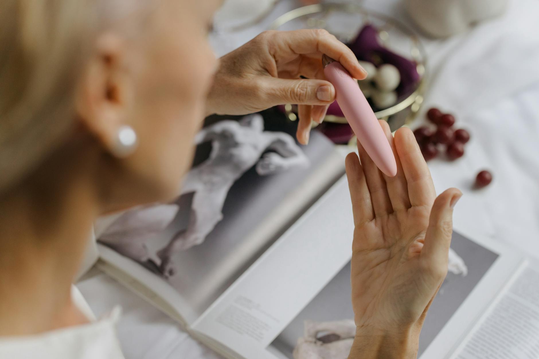 Close-up of a woman holding a pink vibrator with art books nearby, symbolizing reclaiming personal pleasure and intimacy