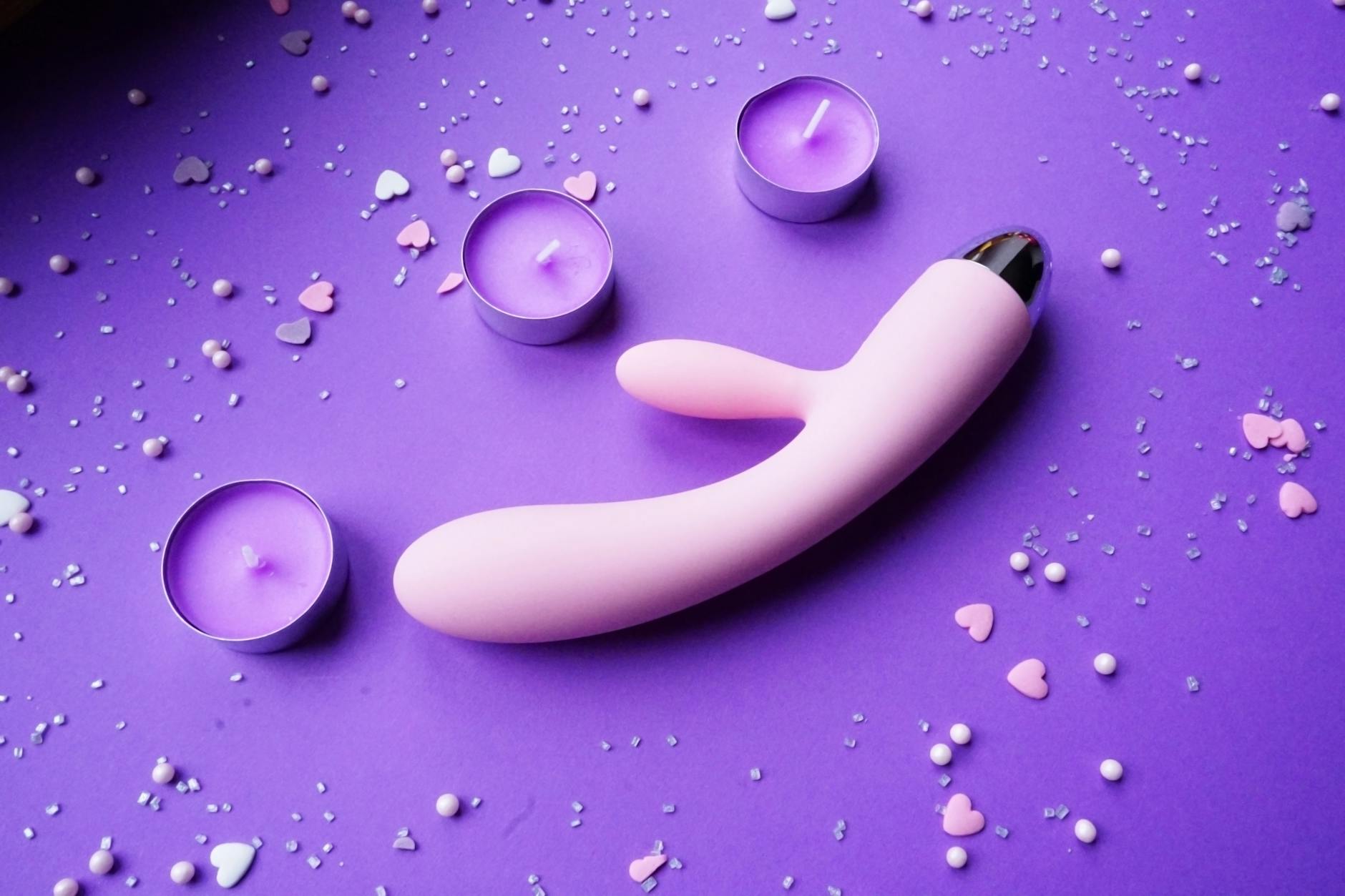 Hand holding an orange vibrator against a minimalistic purple backdrop